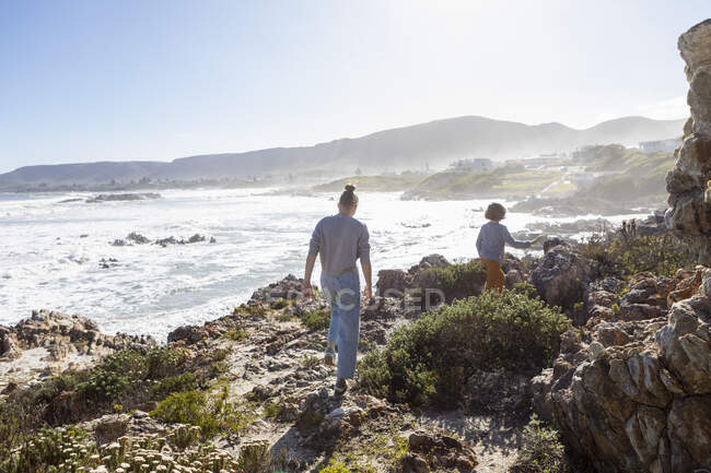 Adolescente y un niño caminando a lo largo de un camino costero sobre el océano. - foto de stock