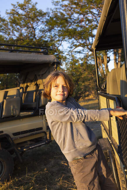 A boy hanging on to the side of a stationary jeep looking at the camera. — Stock Photo