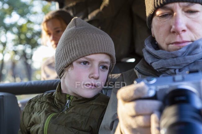 Three people,a boy, girl and mature woman in a vehicle, two looking at a camera screen. — Stock Photo