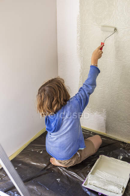 Menino de oito anos usando rolo de tinta para pintar uma parede da casa — Fotografia de Stock