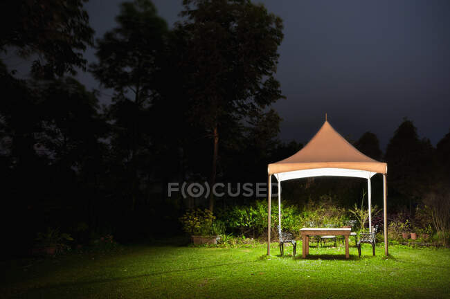 Um pequeno gazebo em um jardim, uma mesa e assento e luzes à noite — Fotografia de Stock