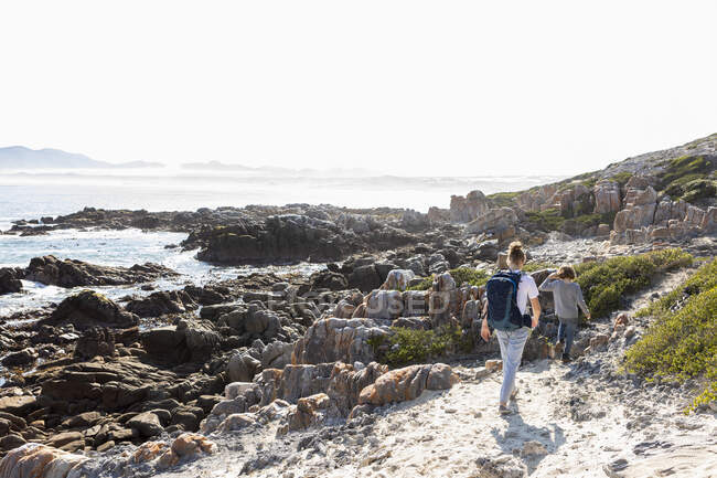 Підліткова дівчинка і молодший брат мандрують узбережною стежкою біля океану. — стокове фото