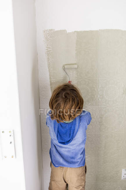 Ragazzo di otto anni che usa il rullo di vernice per dipingere una parete di casa — Foto stock