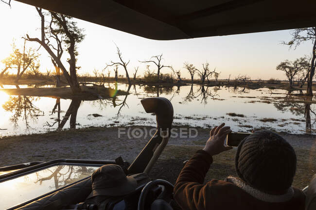 Person sitzt im Jeep und beobachtet den Sonnenaufgang über dem Wasser. — Stockfoto