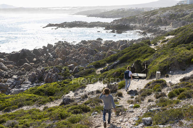 Adolescente y hermano menor senderismo el sendero costero De Kelders, Sudáfrica - foto de stock