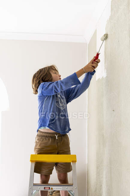 Menino de 8 anos usando rolos de tinta para pintar a parede para decorar uma parede. Decoração de interiores, diy — Fotografia de Stock