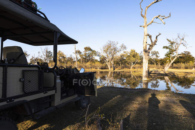 View across flat calm water from a jeep by a waterway, in a wildlife reserve. — Stock Photo