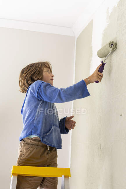 Um menino usando um rolo de tinta para pintar a parede — Fotografia de Stock