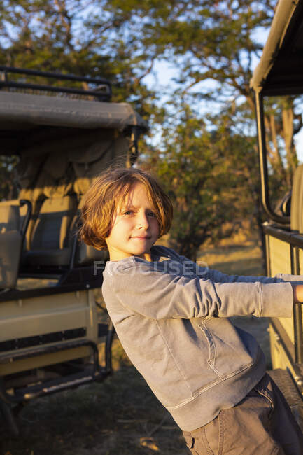 Un garçon accroché au côté d'une jeep fixe regardant la caméra. — Photo de stock