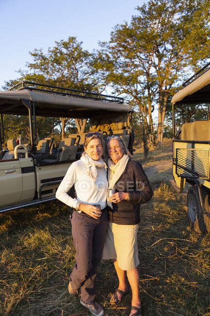 Dos mujeres, una mujer madura y su madre, de pie lado a lado al atardecer en un safari. - foto de stock