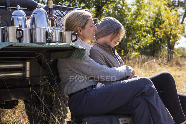 Uma mulher e sua filha adolescente sentados por um jipe — Fotografia de Stock