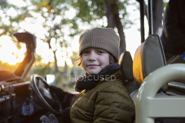 Un niño con sombrero y abrigo en un jeep al amanecer en un safari. - foto de stock