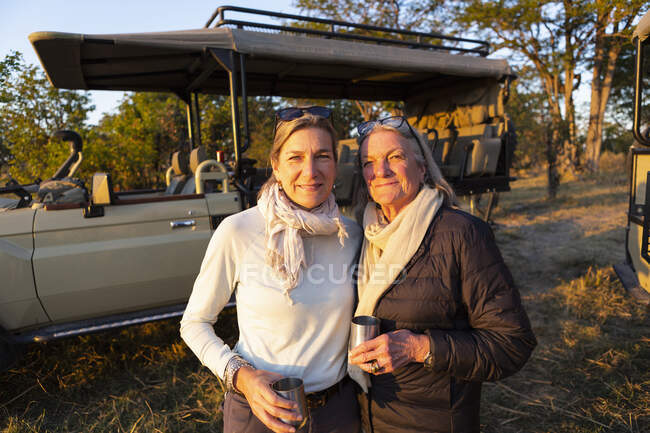 An adult woman and her mother standing side by side, by a jeep at sundown. — Stock Photo