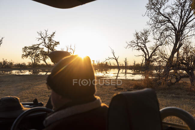 Um motorista em um jipe olhando para o nascer do sol. — Fotografia de Stock