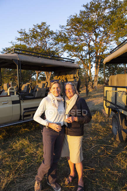 Deux femmes, une femme mûre et sa mère, debout côte à côte au coucher du soleil sur safari. — Photo de stock