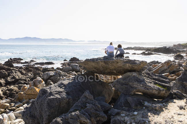 Adolescente y hermano menor haciendo senderismo en un sendero costero junto al océano - foto de stock