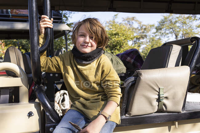 Un ragazzo seduto su una jeep, sorridente, che guarda la macchina fotografica — Foto stock