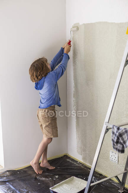 Eight year old boy using paint roller to paint a house wall — Stock Photo