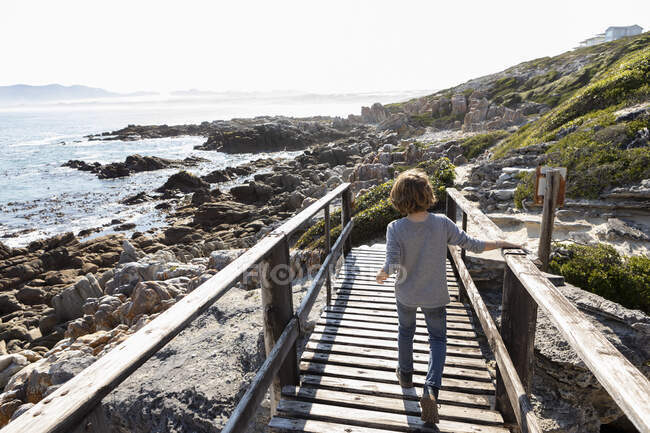 Un niño caminando a lo largo de un paseo marítimo sobre las rocas. - foto de stock