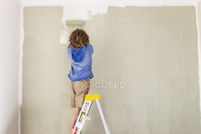 Um menino usando um rolo de tinta para pintar a parede — Fotografia de Stock
