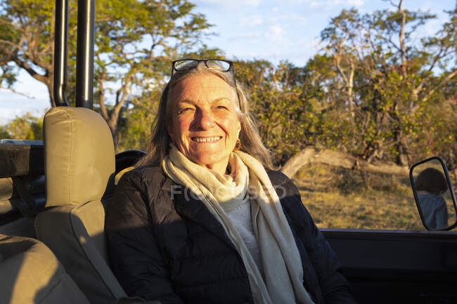 A smiling senior woman seated in a jeep at sunset, smiling. — Stock Photo