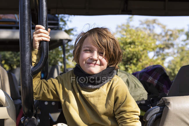 Un chico sentado en un jeep, sonriendo, mirando a la cámara - foto de stock