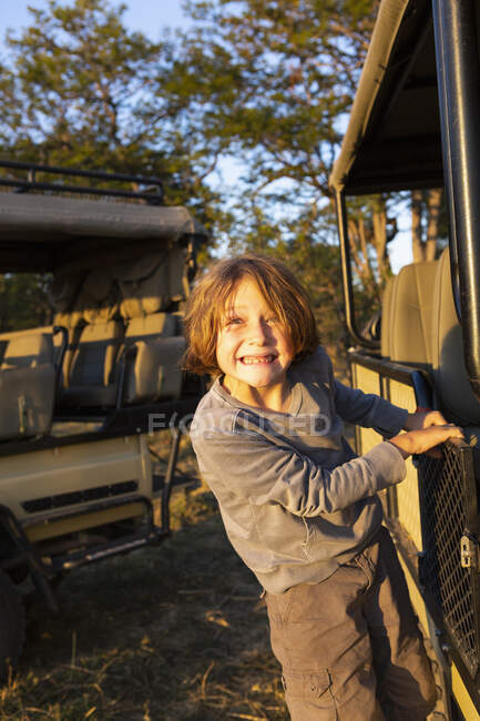 Un chico colgado del lado de un jeep estacionario mirando a la cámara. - foto de stock
