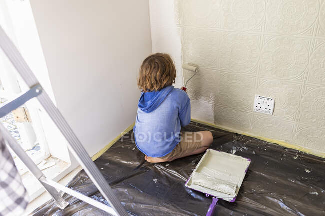 Menino de oito anos usando rolo de tinta para pintar uma parede da casa — Fotografia de Stock