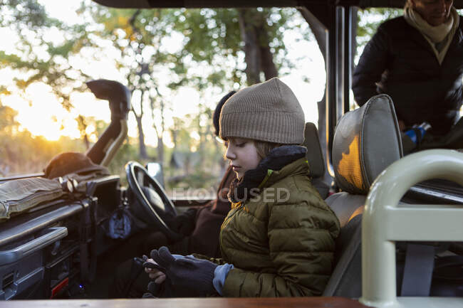 Un niño con sombrero y abrigo en un jeep al amanecer en un safari. - foto de stock