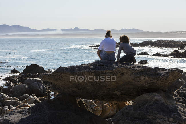 Adolescente y hermano menor haciendo senderismo en un sendero costero junto al océano - foto de stock