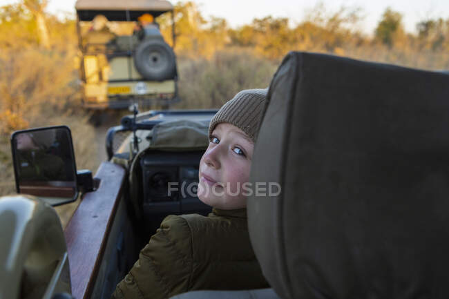 Ein Junge mit Hut und Mantel im Jeep bei Sonnenaufgang auf Safari. — Stockfoto
