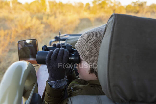 Kleiner Junge im Jeep mit Fernglas, Fahrt im Morgengrauen durch den Busch. — Stockfoto