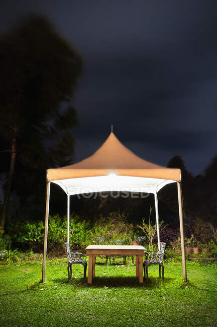 Un pequeño mirador en un jardín, una mesa y un asiento y luces por la noche - foto de stock