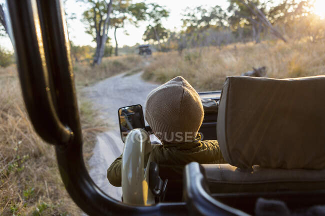 Um menino sentado em um jipe em uma viagem de safári ao nascer do sol. — Fotografia de Stock