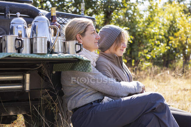 A woman and her teenage daughter sitting by a jeep — Stock Photo
