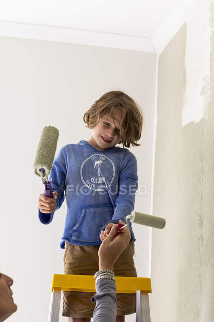 Mère et son garçon de 8 ans utilisant des rouleaux de peinture pour peindre le mur — Photo de stock