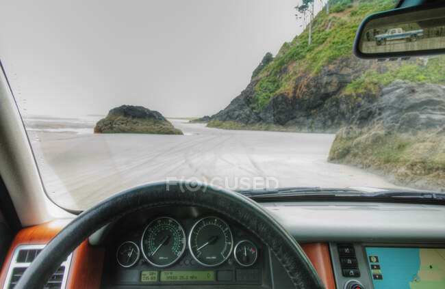 Beach seen from driver's seat of a car, with steering wheel in foreground. - foto de stock