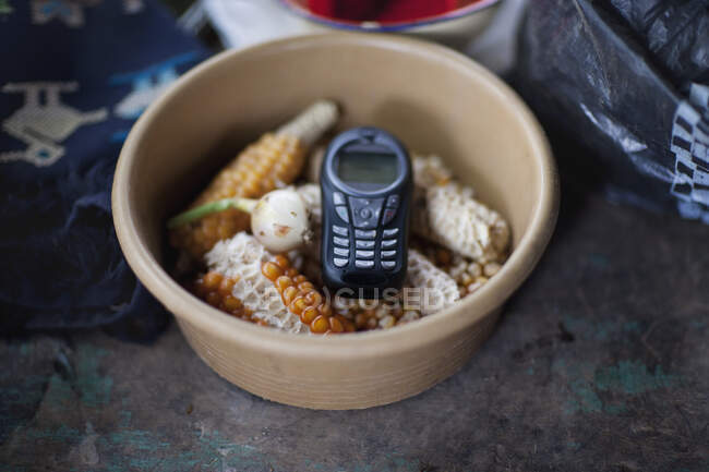 A cell phone,mobile communications,a handset or telephone,in a bowl of maize kernels. - foto de stock