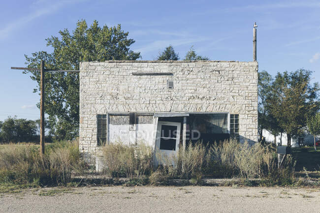 Old store with broken door and windows, sage brush and weeds growing on the forecourt. — Photo de stock