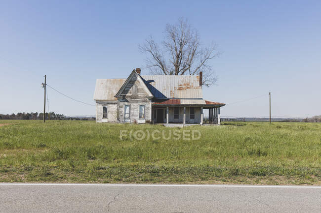Брошенный дом с ржавой крышей на ферме по дороге. — стоковое фото