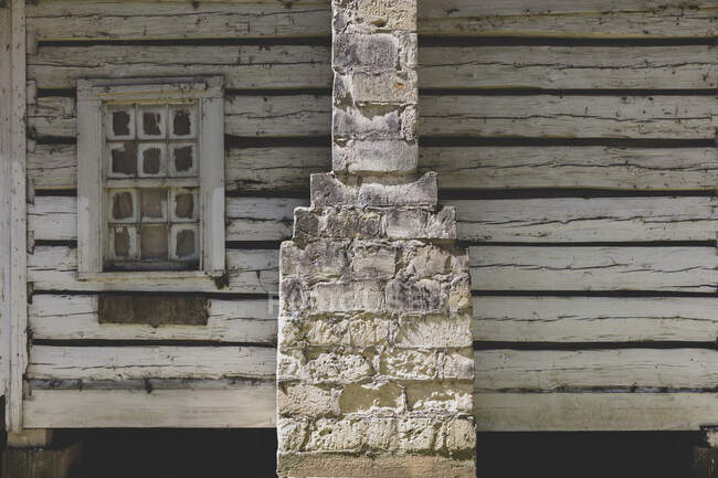 Ein verlassenes Blockhaus mit einem steinernen Schornstein, rissiger und vertrockneter Holzverkleidung und zerbrochenem Fenster. — Stockfoto