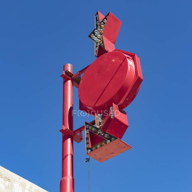Un panneau publicitaire avec des flèches et des lumières sur un poteau contre le ciel bleu. — Photo de stock