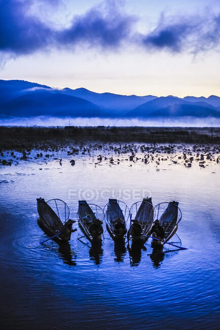 A group of fishermen on Lake Inle at dusk, mist rising from the water. — Foto stock