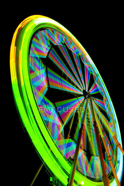 Fairground ferris wheel with lights in rainbow colours, against a black sky. — Stock Photo