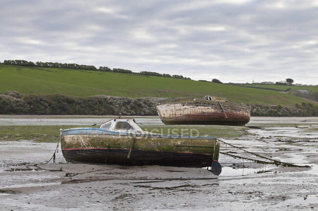 Dos barcos varados en marea baja, con cascos fangosos y líneas de amarre deshilachadas - foto de stock