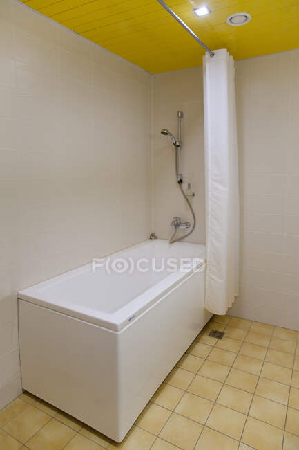 Um banheiro, banheira e parede chuveiro montado e cortina de chuveiro, piso em azulejo e teto amarelo. — Fotografia de Stock