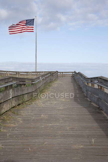 Boardwalk through grassland with mountains and American flag flying. — Stock Photo