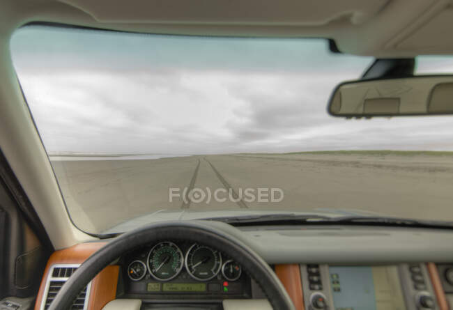 Beach and cliffs seen from driver's seat of a car, with steering wheel in foreground. - foto de stock