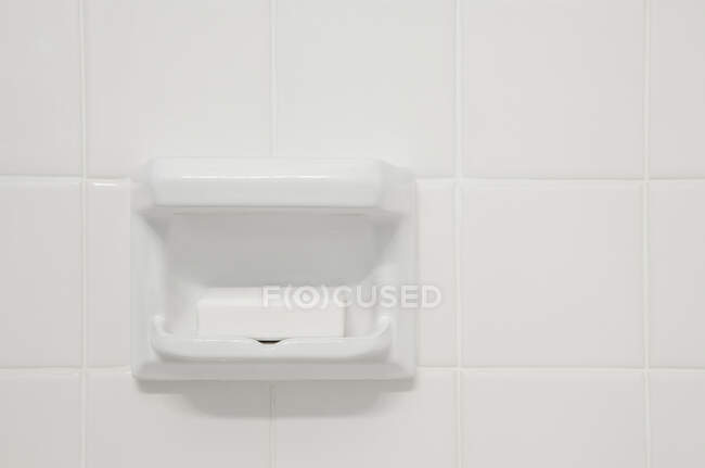 A white tiled wall of a bathroom or shower room,with a shaped porcelain recess. A block of soap. — Photo de stock