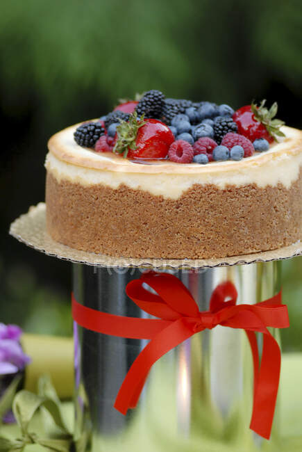A cake with icing and fresh berries and a red ribbon. - foto de stock